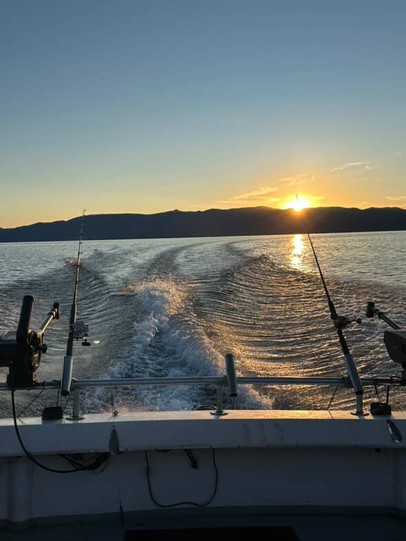 Boat wake at sunset with fishing rods and distant mountains.