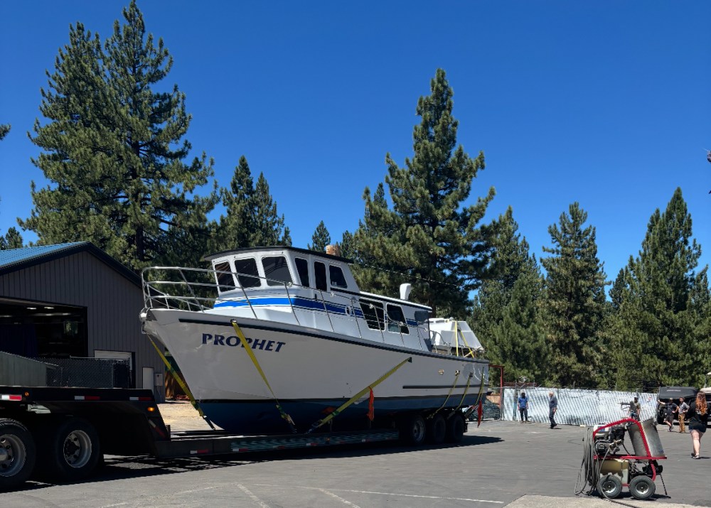 Large boat named 'Prophet' on a trailer surrounded by trees and people.