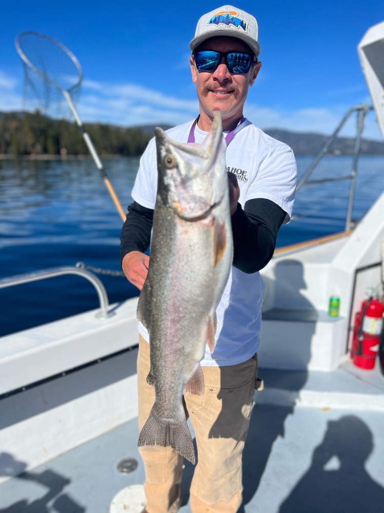 Man on boat holding large fish with a fishing net in the background.