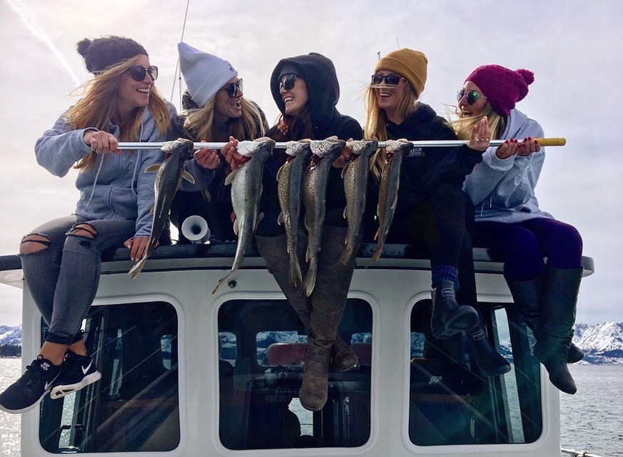 Five people sit on a boat holding a rod with several fish.