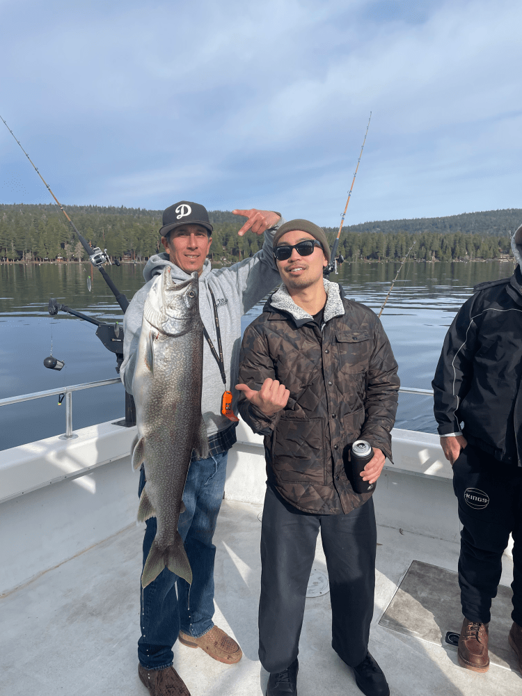 Two people on a boat, one holding a large fish, with fishing rods in the background.