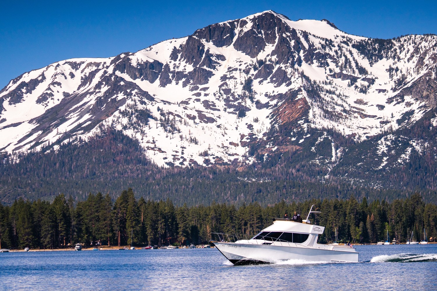 Boat on lake with snowy mountain and pine trees in background.