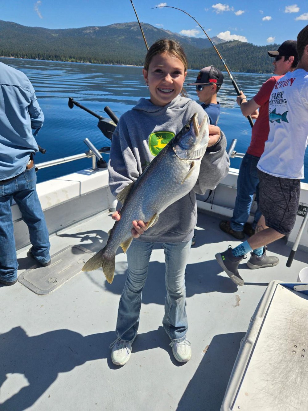 Young girl on a boat holding a large fish with others fishing behind her.