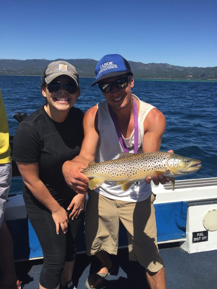 Man holding a fish on a boat with a woman sitting beside him.